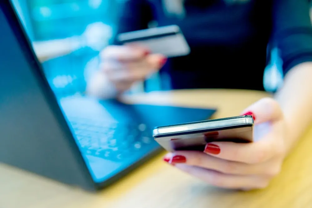 Cliente réglant en ligne les frais d'expédition de son objet trouvé, carte bancaire et smartphone en main