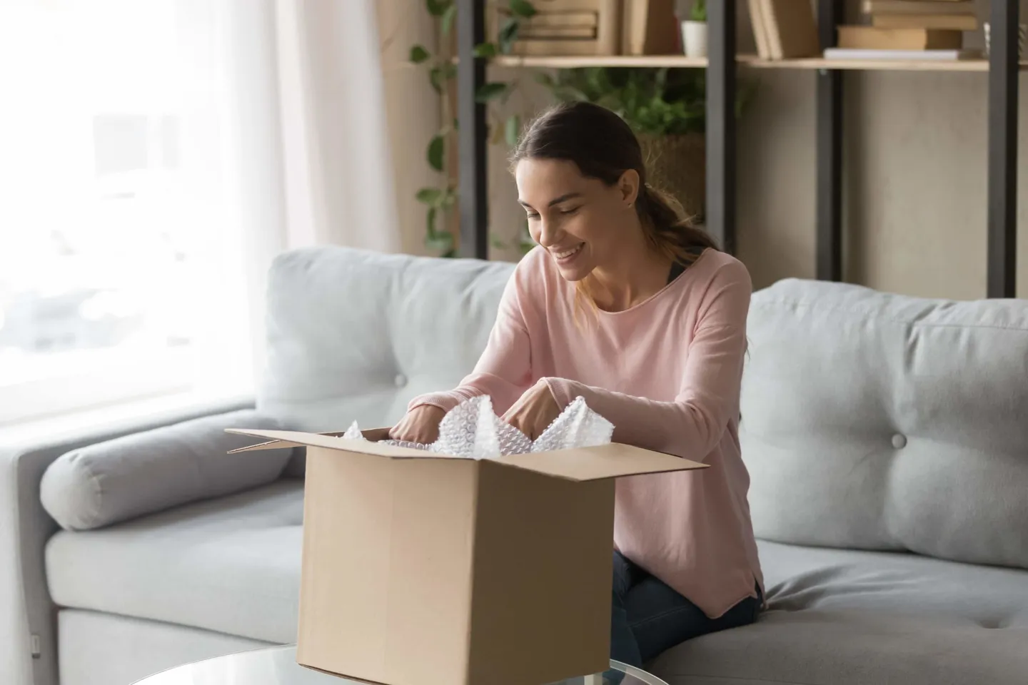Cliente souriante ouvrant chez elle le colis contenant son objet oublié
